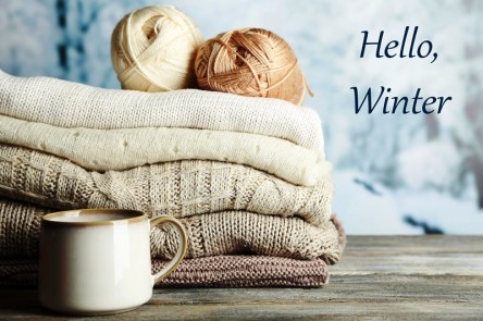 Cup of hot drink, knitting clothes and yarn on light winter background