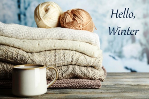 Cup of hot drink, knitting clothes and yarn on light winter background
